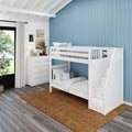 White wooden bunk bed with stair-storage against a blue shiplap accent wall in a modern kids' bedroom with white dresser, lamp, houseplants and jute rug