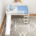 Overhead view of a white wooden kids loft bed with slide and ladder, blue quilted mattress, star-pattern sheets and colorful pillows in a modern children's bedroom with geometric rug.
