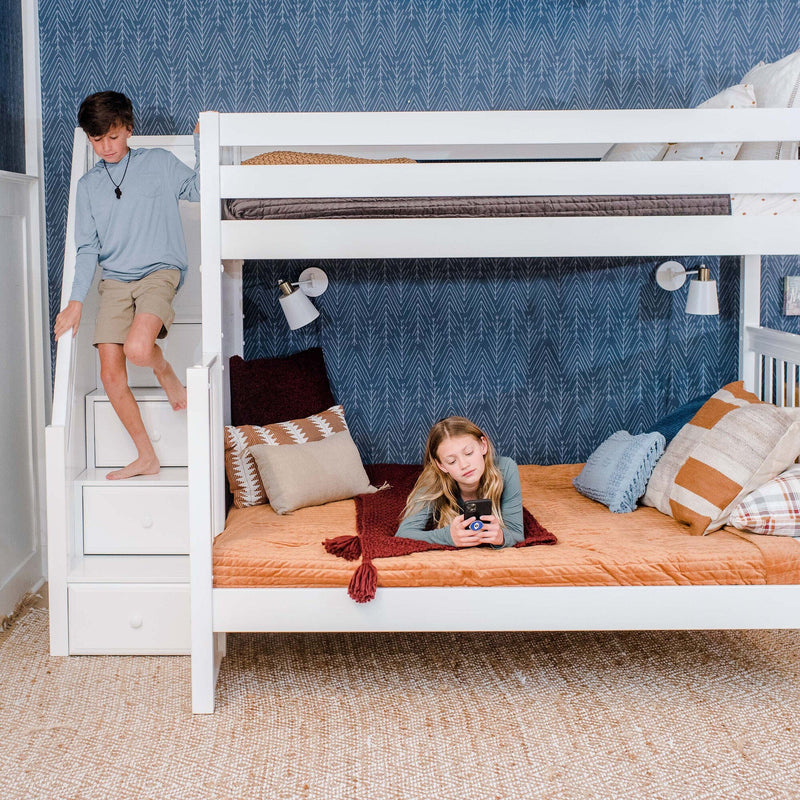 Modern kids' bedroom with white bunk bed and built-in storage stairs, navy patterned wallpaper, orange quilted bedding, decorative pillows and wall-mounted reading lights