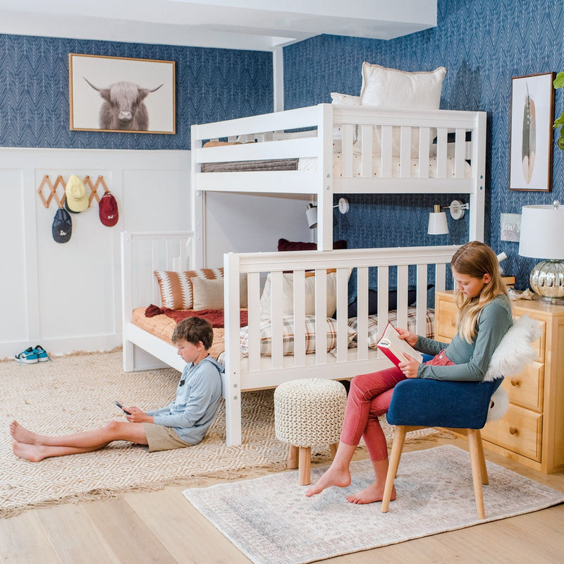 Cozy kids' bedroom with white wooden bunk bed, blue chevron wallpaper, knit pouf and textured rugs, two children reading and using a mobile device