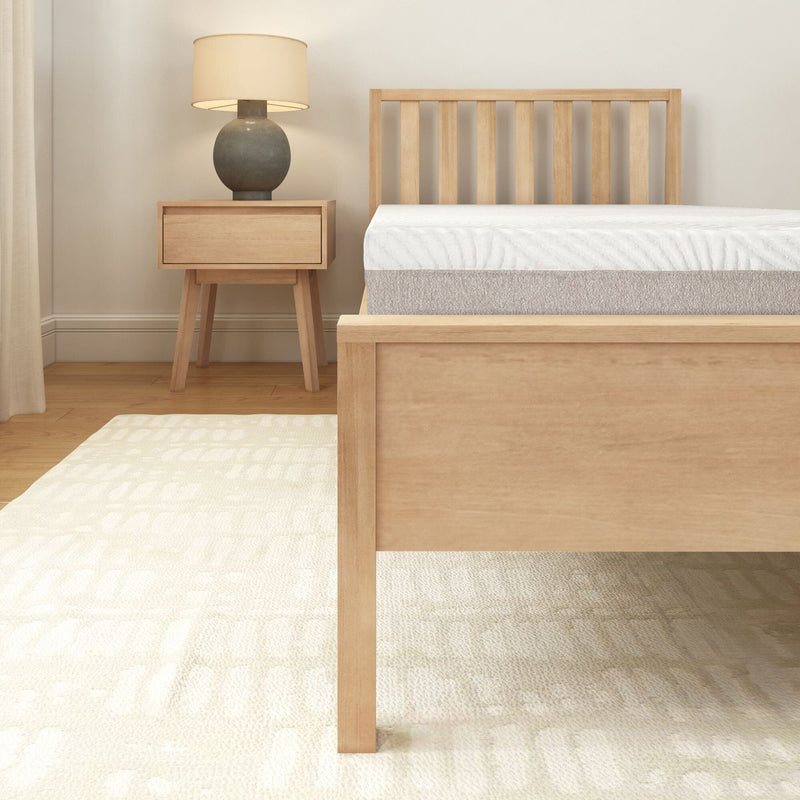 Modern minimalist bedroom with wooden bed frame, white mattress, matching nightstand, lamp, and light-colored rug.