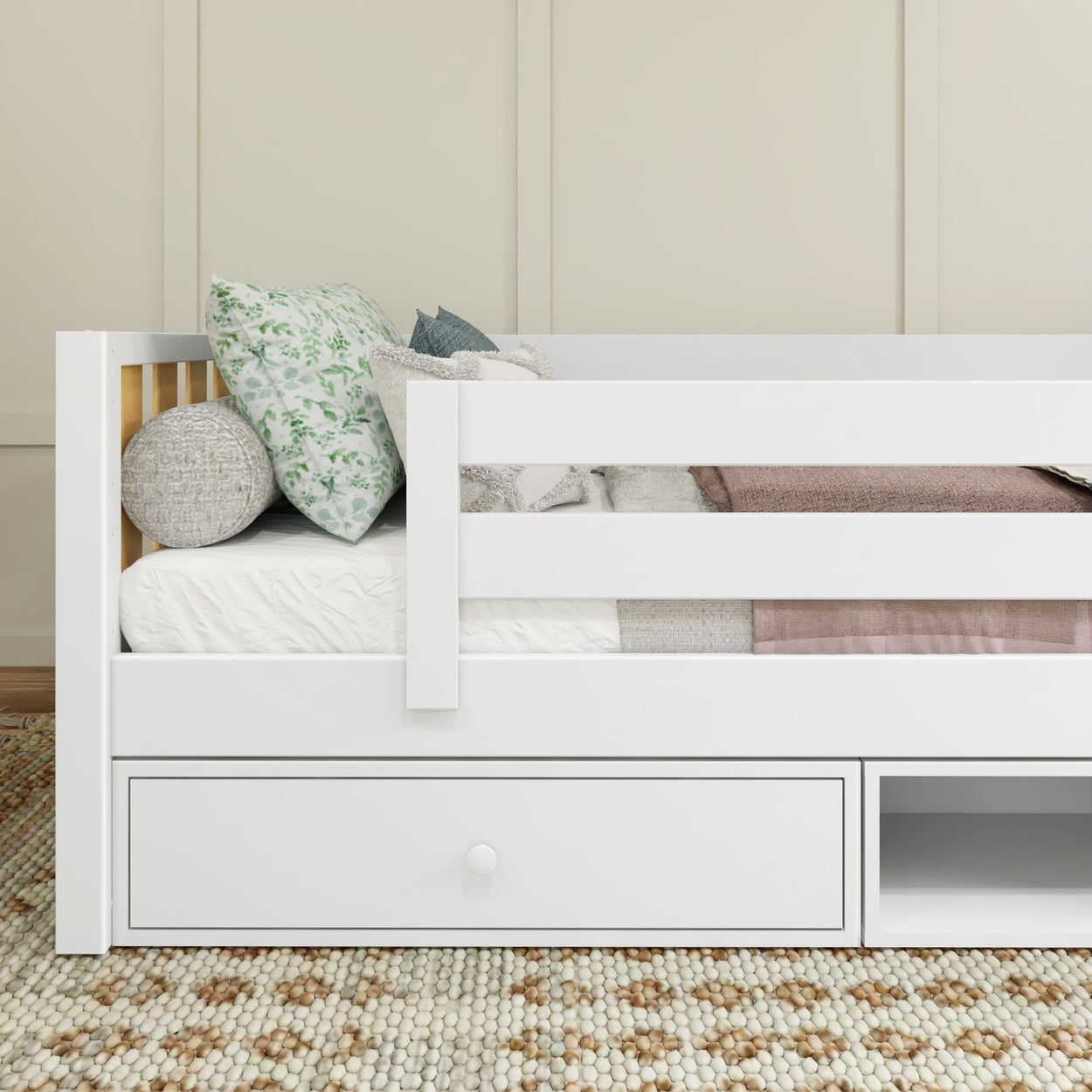 White children's bed with storage drawer, patterned pillows, and cozy blanket in a modern kids' bedroom.