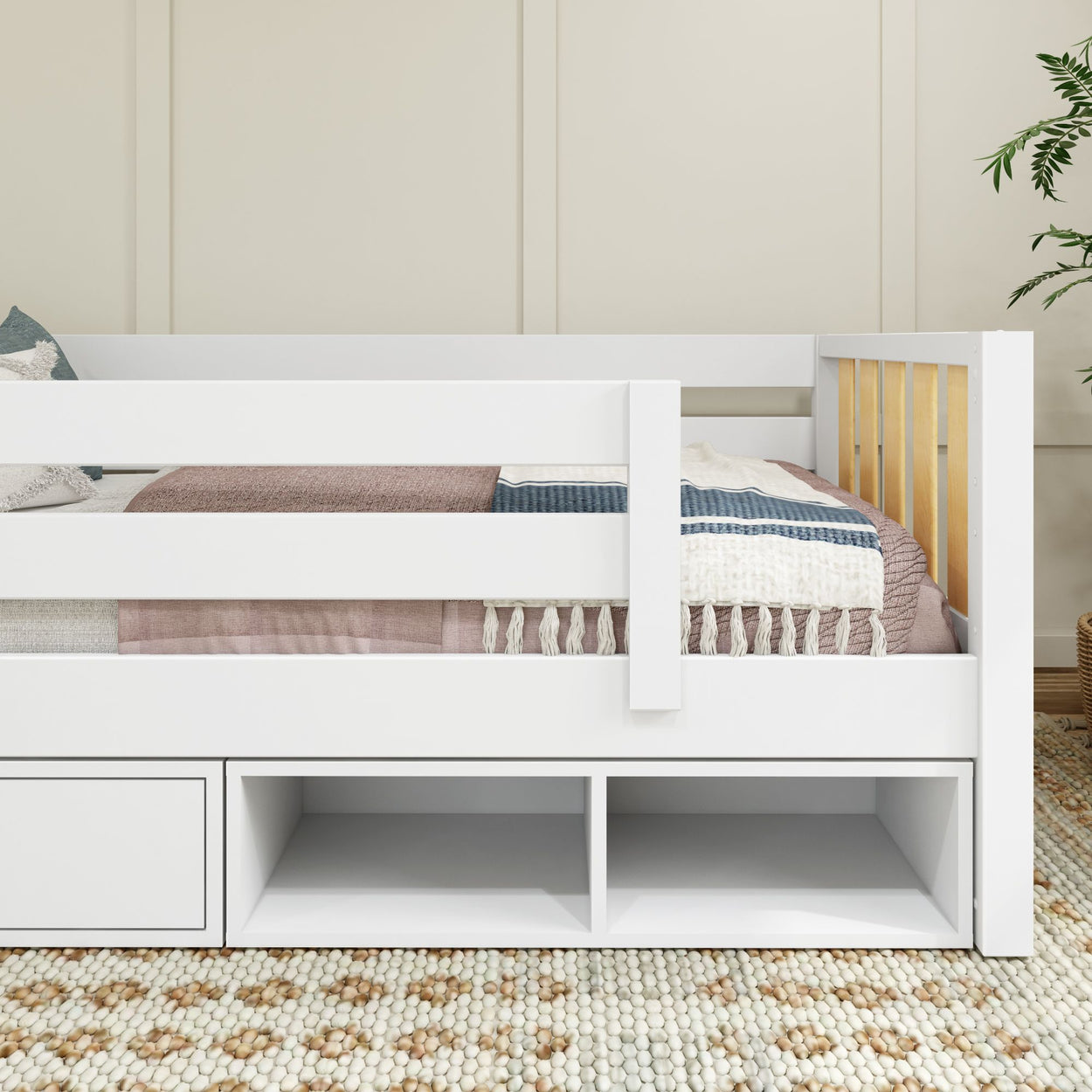 White toddler bed with safety rails and under-bed storage drawers, placed on a patterned carpet in a cozy room setting.