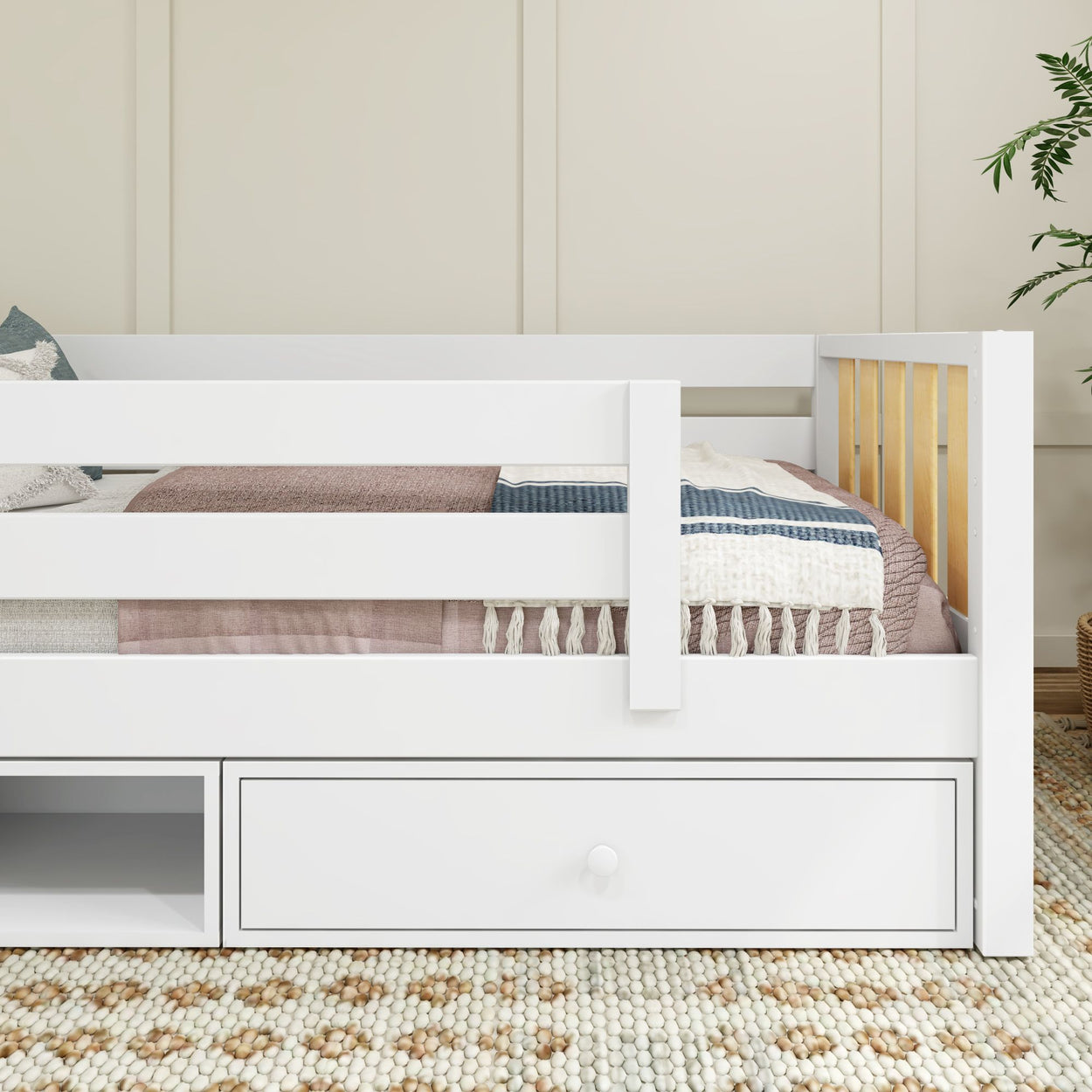 White wooden bed with storage drawer, cozy throw pillows, and textured rug in a modern bedroom setting.