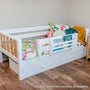 White wooden toddler bed with built-in storage drawers, colorful tropical quilt, plush flamingo and book-organizer pocket, mustard throw in modern nursery