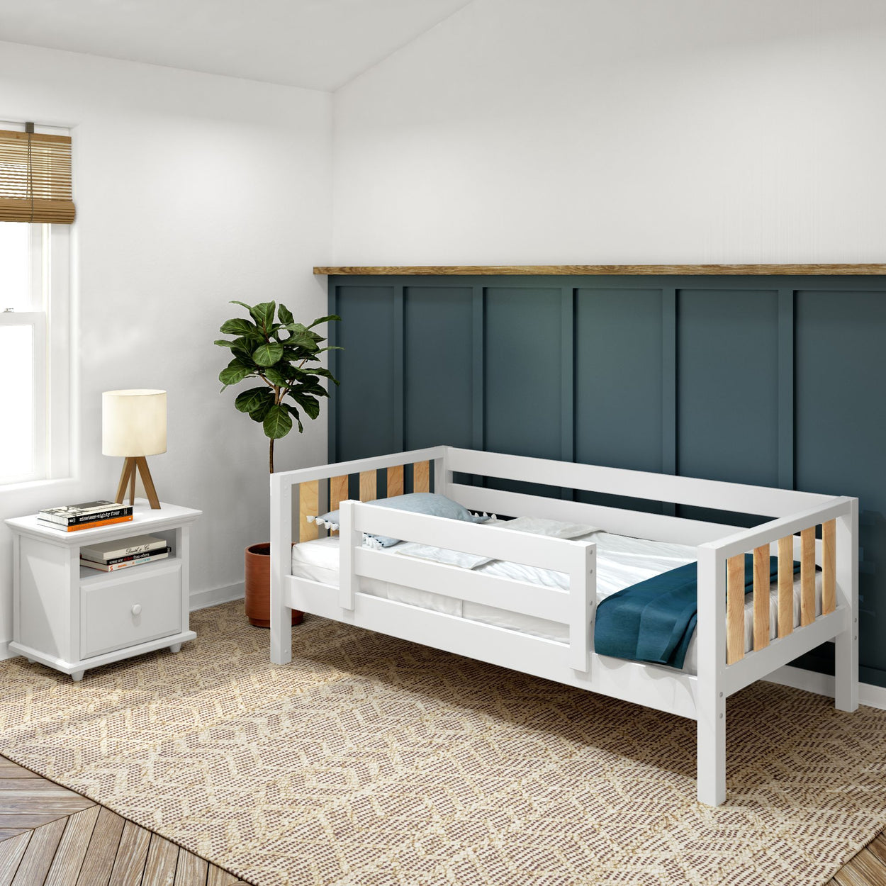 White toddler bed with safety rails in a modern kids room featuring a green accent wall, woven rug, and bedside table with a lamp and books.