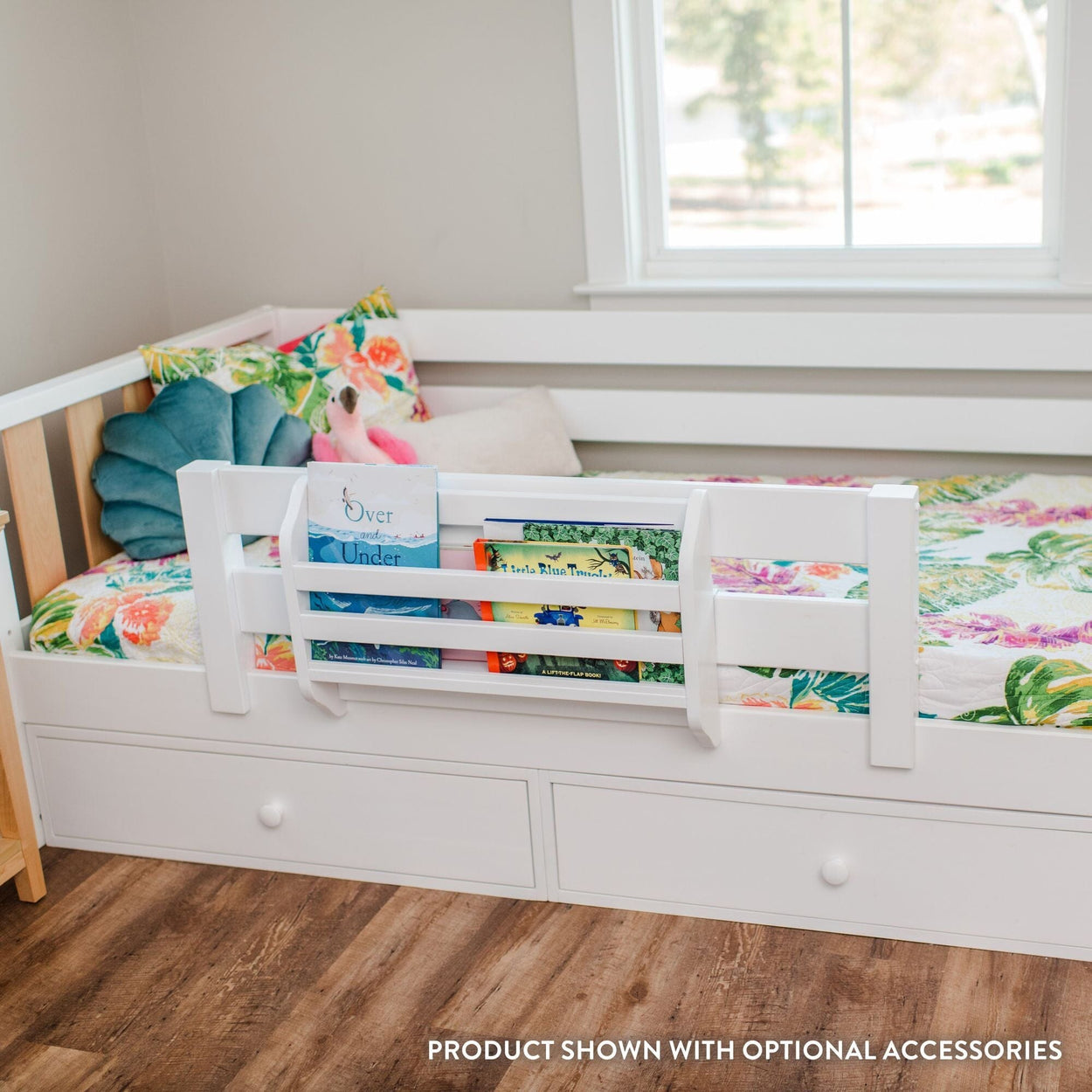 White toddler bed with built-in book rack and under-bed storage drawers, floral kids bedding and plush toys by a sunlit window
