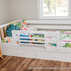White toddler bed with built-in book rack and under-bed storage drawers, floral kids bedding and plush toys by a sunlit window