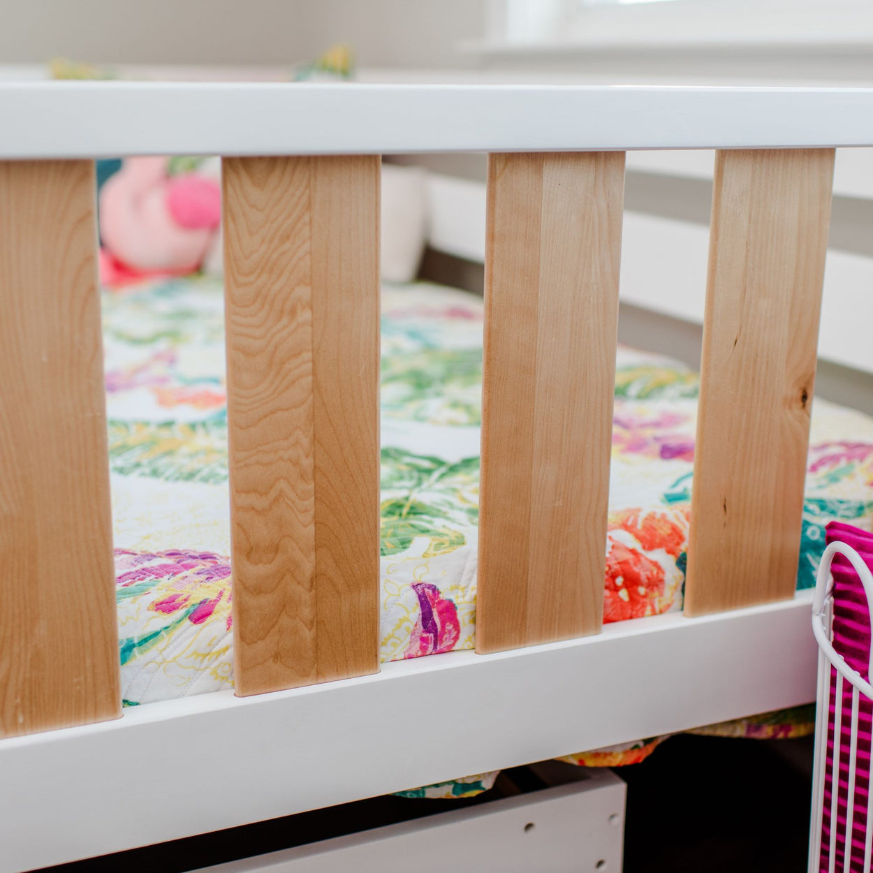 Close-up of a colorful toddler bed with wooden rails and a floral quilt in a child's bedroom.