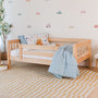 Wooden toddler bed in airy kids bedroom nursery with blue duvet, vehicle-themed bedding and wall decals, striped yellow rug and teddy bear