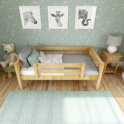 Wooden toddler bed in a cozy nursery with animal-themed decor on mint green walls.