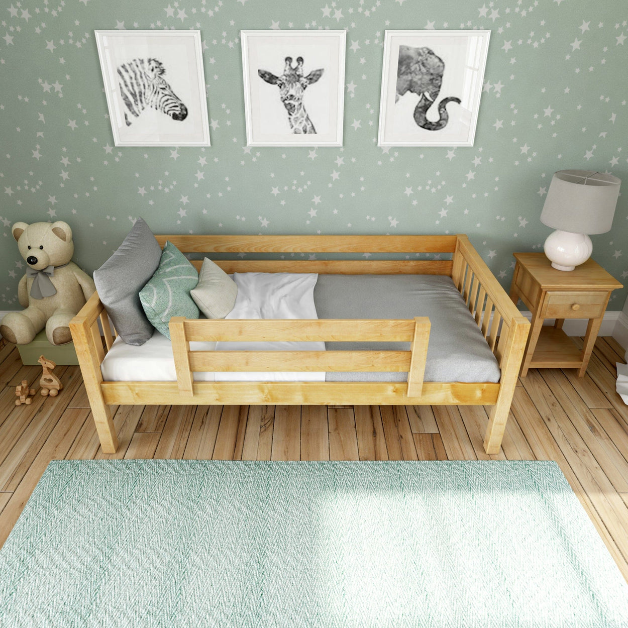 Light wooden toddler bed in cozy kids bedroom with green star wallpaper, framed animal wall art, plush teddy, bedside table and mint rug — nursery decor