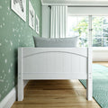 White toddler bed headboard against mint green star wallpaper in a bright nursery with framed animal prints, gray pillow, white curtains, hardwood floor and teal rug