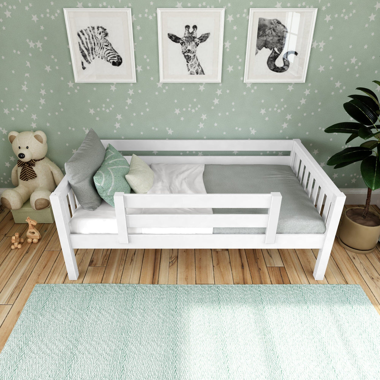 White wooden toddler bed with safety rail in a mint-themed nursery, star-pattern wallpaper, animal wall art, plush teddy bear, hardwood floor and mint area rug