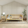 Neutral farmhouse nursery with wooden toddler bed, board-and-batten accent wall, bedside table and lamp, boho woven rug and potted plant