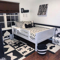 Black and white kids bedroom with white wooden bed, monochrome bedding, alphabet foam floor mats, panda plush and "Color Outside the Lines" wall art
