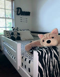 Black-and-white themed kids bedroom with white daybed, polka-dot bedding, zebra-print throw, stuffed panda and large plush dog, "Dream" wall sign and window light.