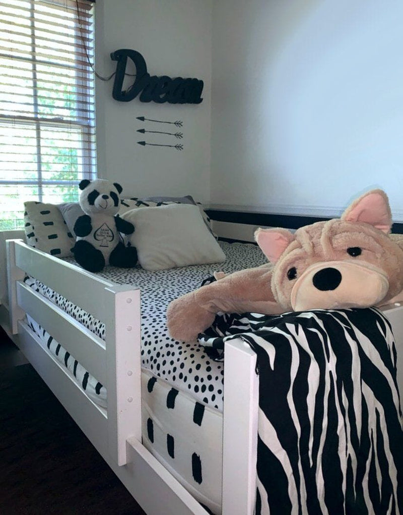 Black-and-white themed kids bedroom with white daybed, polka-dot bedding, zebra-print throw, stuffed panda and large plush dog, "Dream" wall sign and window light.