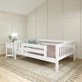 Neutral nursery interior with white wooden toddler bed and safety rails, beige board-and-batten walls, green ceramic lamp, pastel pillows and textured woven rug